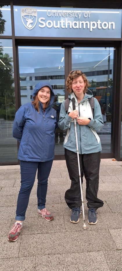 Two women standing in front of a glass door with University of Southampton written on top of the door. The women on the right has a walking stick in her hand. 