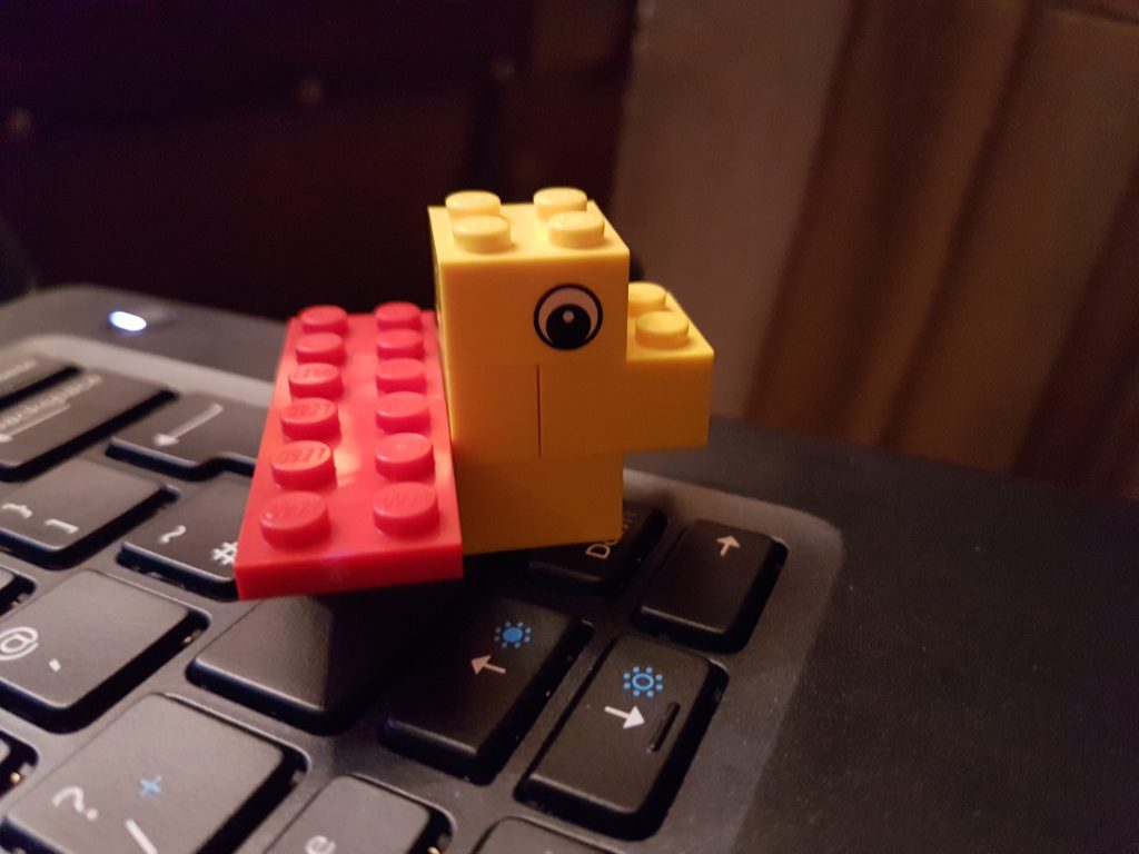 A small lego duck resting on a laptop keyboard.