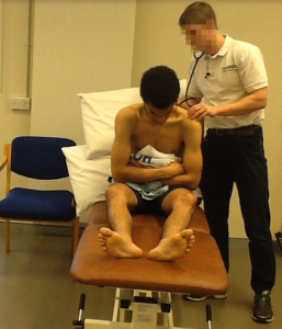A student using a stethoscope on a patient sitting on a bed as part of an OSPE examination.