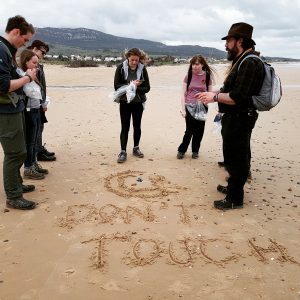 People standing on a beach looking at a jelly fish. The words Do Not Touch are written in the sand. 