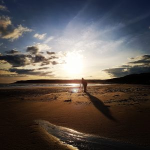 Beach at sunset with a person in the foreground with a camera on a tripod