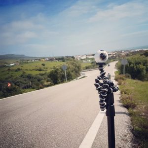 A camera on a tripod on another tripod by a roadside. 