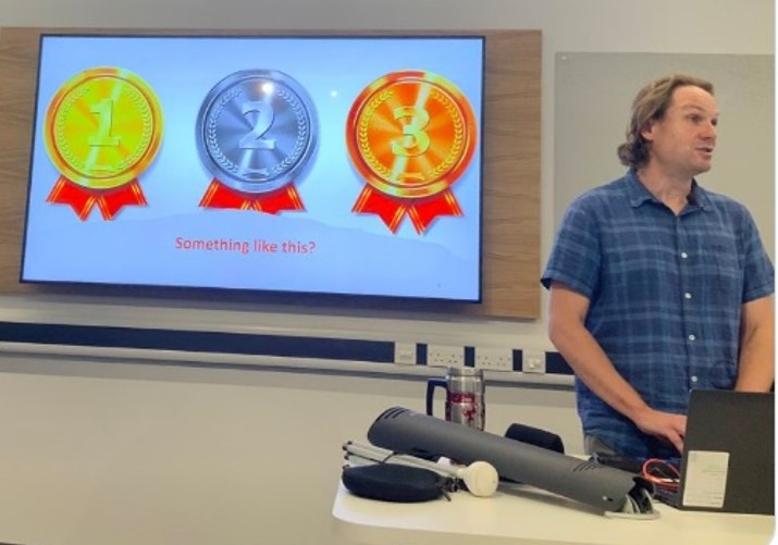 An image with Ben presenting a slide showing the bronze, silver, gold medals. 