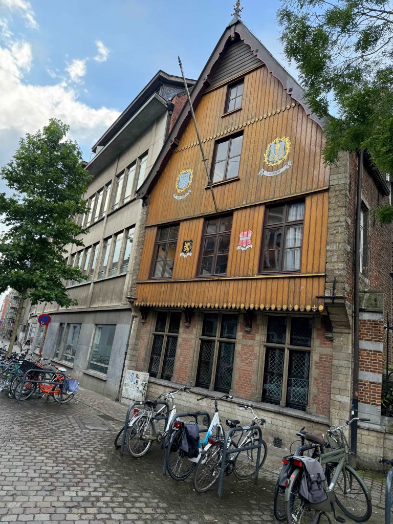 An image showing two adjacent buildings. The one in focus has a wood panel in the front and several bicycles parked along the street.