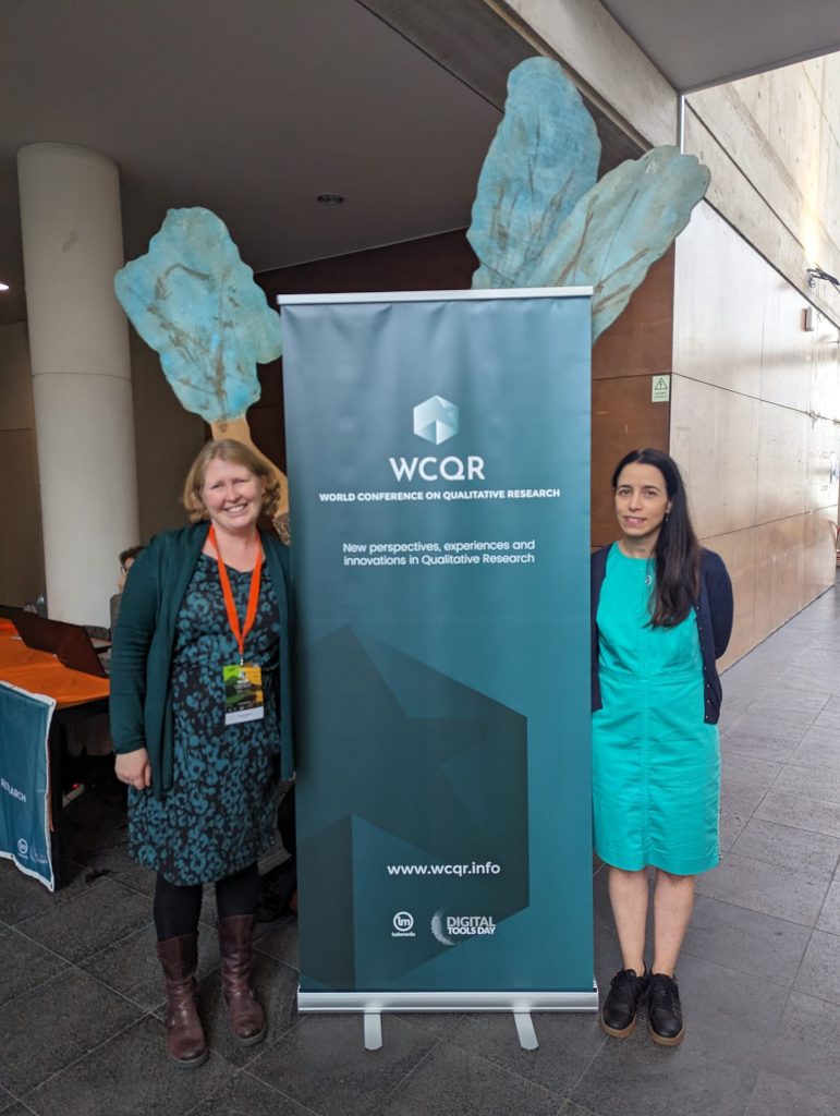 Two women standing on two sides of a  sign board of WCQR, at the University of the Azores for the WCQR.