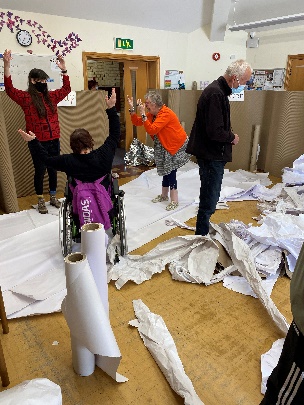 Research participants and arts practitioner, arms aloft, sharing the pleasure of paper materials.