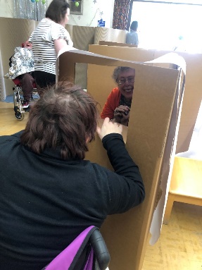 Participants peeping through two sides of a cardboard box, enjoying the activity.