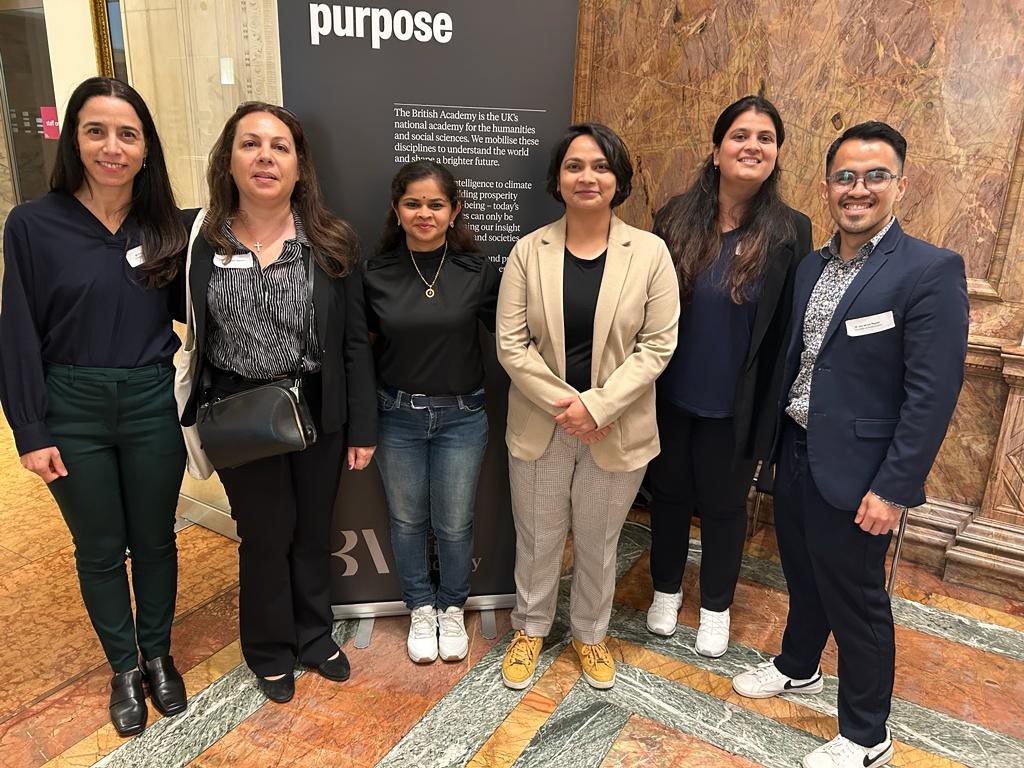 A group photo of 6 people in front of the conference poster