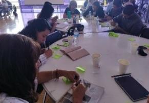 Several people sat around round tables, writing on sticky notes