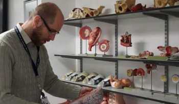 Scott Border is pictured studying an anatomy model, with a further selection on shelves behind him.