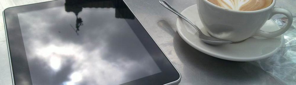 A tablet and a cup of coffee on a table.