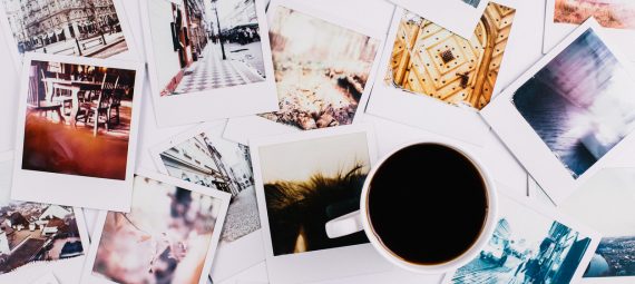 A mug with coffee standing between a bunch of polaroids.