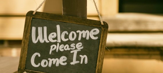 A blackboard sign with Welcome please come in, written on it.