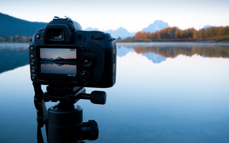 Camera on tripod filming a view of a lake and mountains