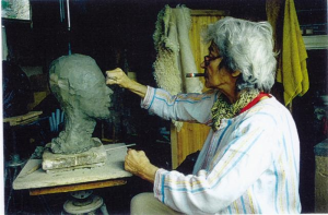 Fiore de Henriques is shaping a clay bust with their hands.