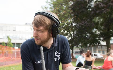 A media producer is holding a microphone and listening through headphones.