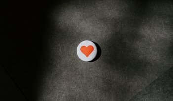 A circle pin badge with a red heart resting on a black surface.