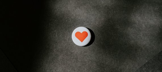 A circle pin badge with a red heart resting on a black surface.