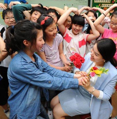 A teacher and her students, with some of the students holding flowers showing their appreciation and respect for their teacher.