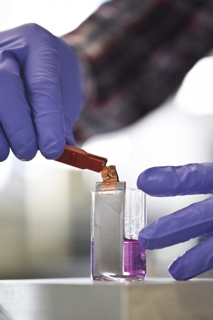 A hand hooks up an electrode to coat something conductive in gold, using electricity