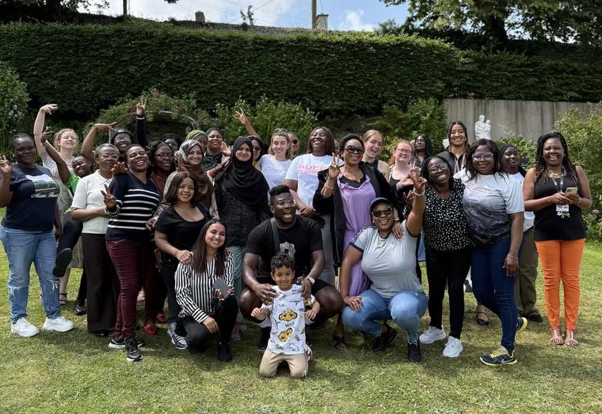 A picture of a group of about 30 happy people (mainly, but not only, women) of different races, religions, and ages in a sunny garden, smiling at the camera and having a good time.