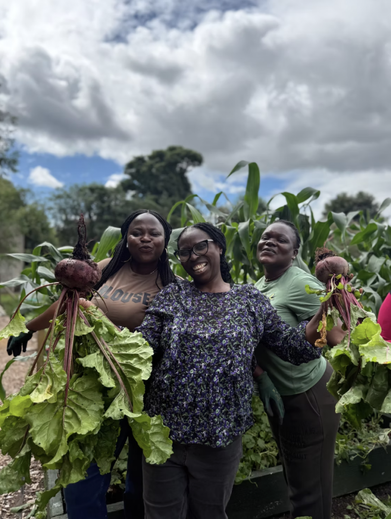 3 women smiling at the camera while holding produce from the international garden.