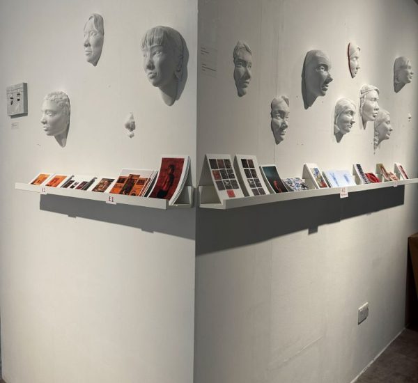 White sculpted faces are mounted on two adjoining walls above shelves displaying small colorful prints and booklets.