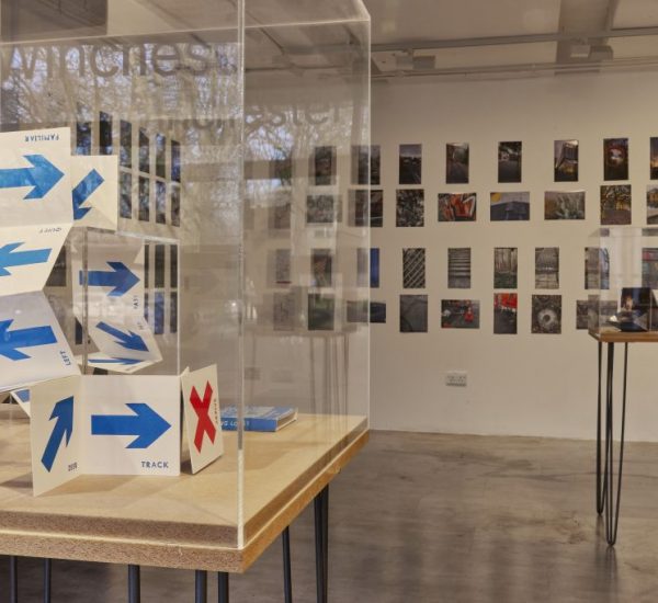 An art gallery display features a folded paper structure marked with blue arrows and a red