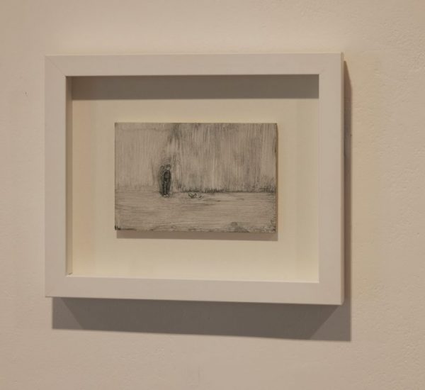A small monochrome artwork in a white frame depicts a textured scene with a solitary figure, mounted on a plain wall.
