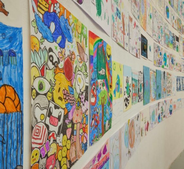 Another close-up of the wall highlights bright, detailed illustrations of animals, plants, and ocean life among other imaginative designs. The artworks are arranged in rows along the curved gallery space.