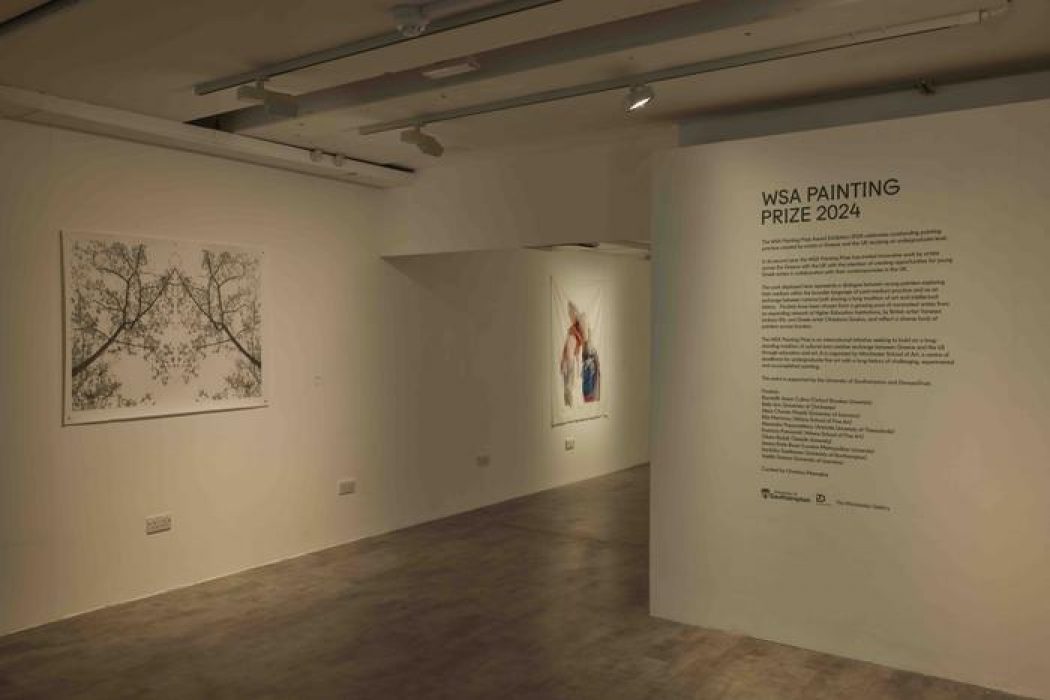 A gallery wall displays the WSA Painting Prize 2024 text alongside two artworks: one featuring delicate tree branches and another with abstract colorful forms. The space is softly lit with neutral walls and a polished floor.