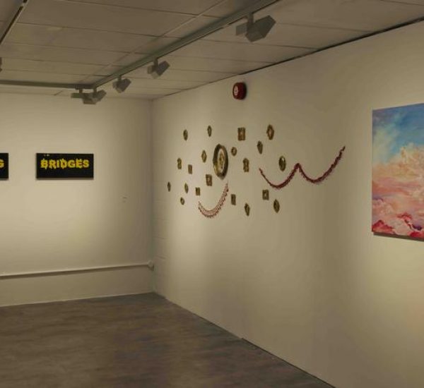A gallery wall displays two black-and-yellow text artworks reading “Burning Bridges,” a colorful abstract painting of clouds, and a decorative arrangement of small framed pieces with red garlands.